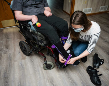 Direct Care professional is putting AFO leg brace on person with disability. Allowing them to gain experience in patient care which helps them get into occupational therapy school.